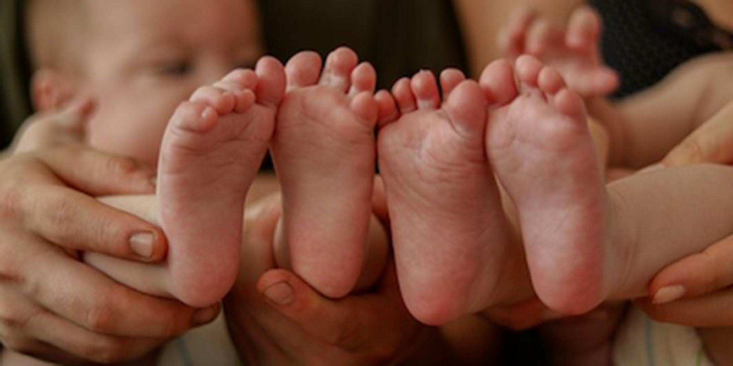 To babyer har fødderne helt tæt på kameraet. I baggrunden kan man se mødrene, der holder babyerne,
